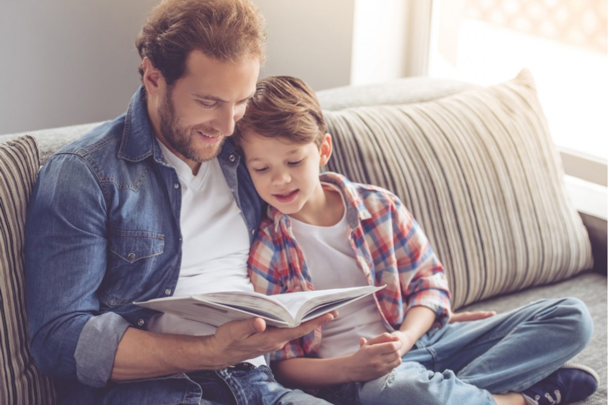 Father and son reading a book together on a sofa