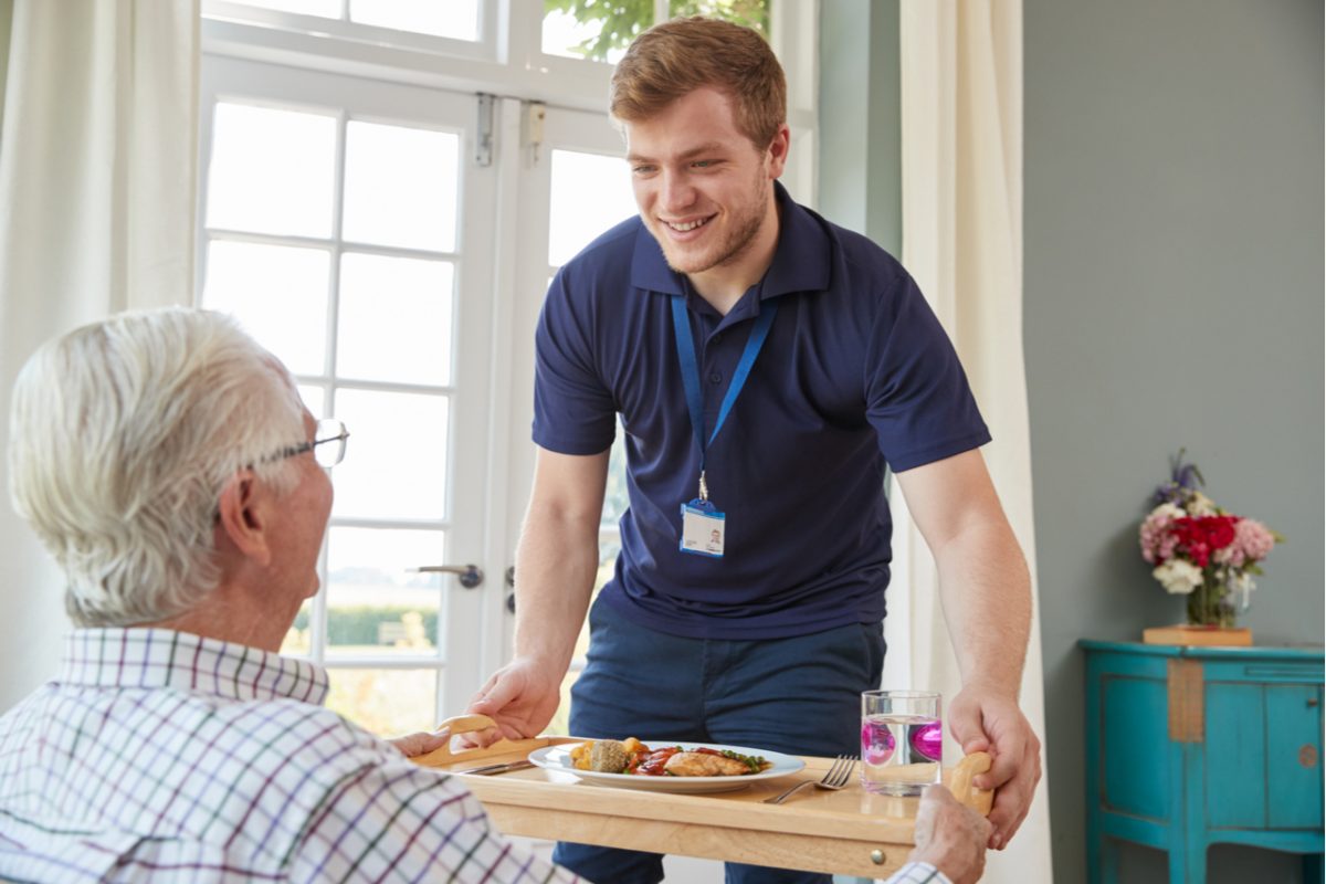 A care worker serving dinner to an older man