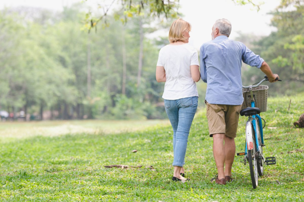 Senior couple walking through the park and pushing a bike