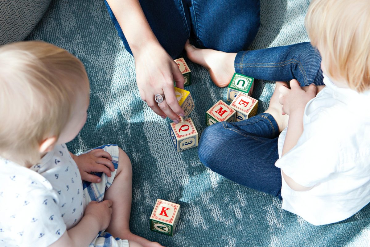 Two young children playing with wooden blocks with their mother