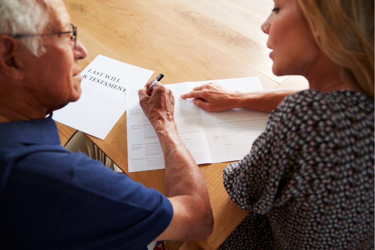 A woman helping an older man complete his will.