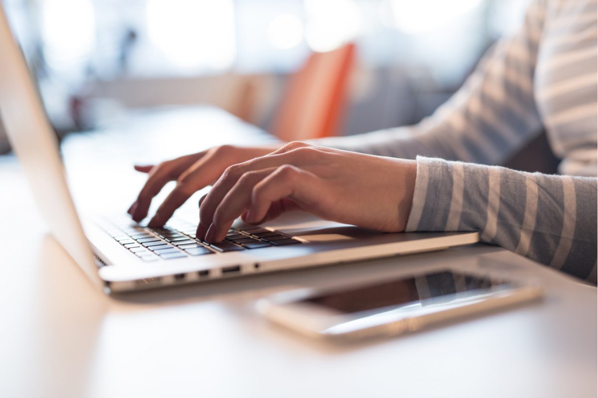 A young woman typing on a laptop in an office space.