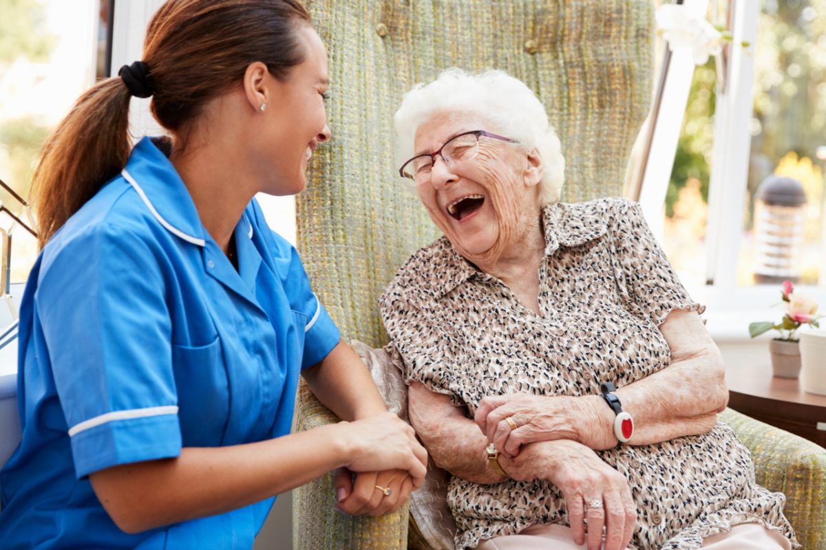An older woman laughing and talking with a nurse.