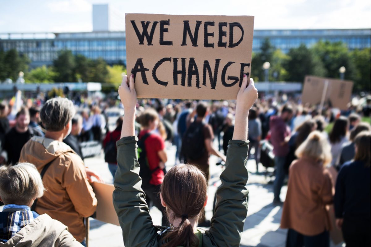 A group of protesters with a sign that says, “we need a change”.