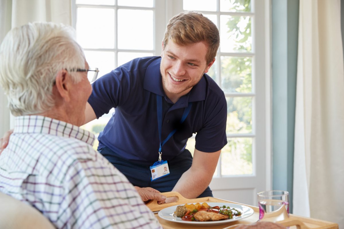 A care worker serving an older man dinner.