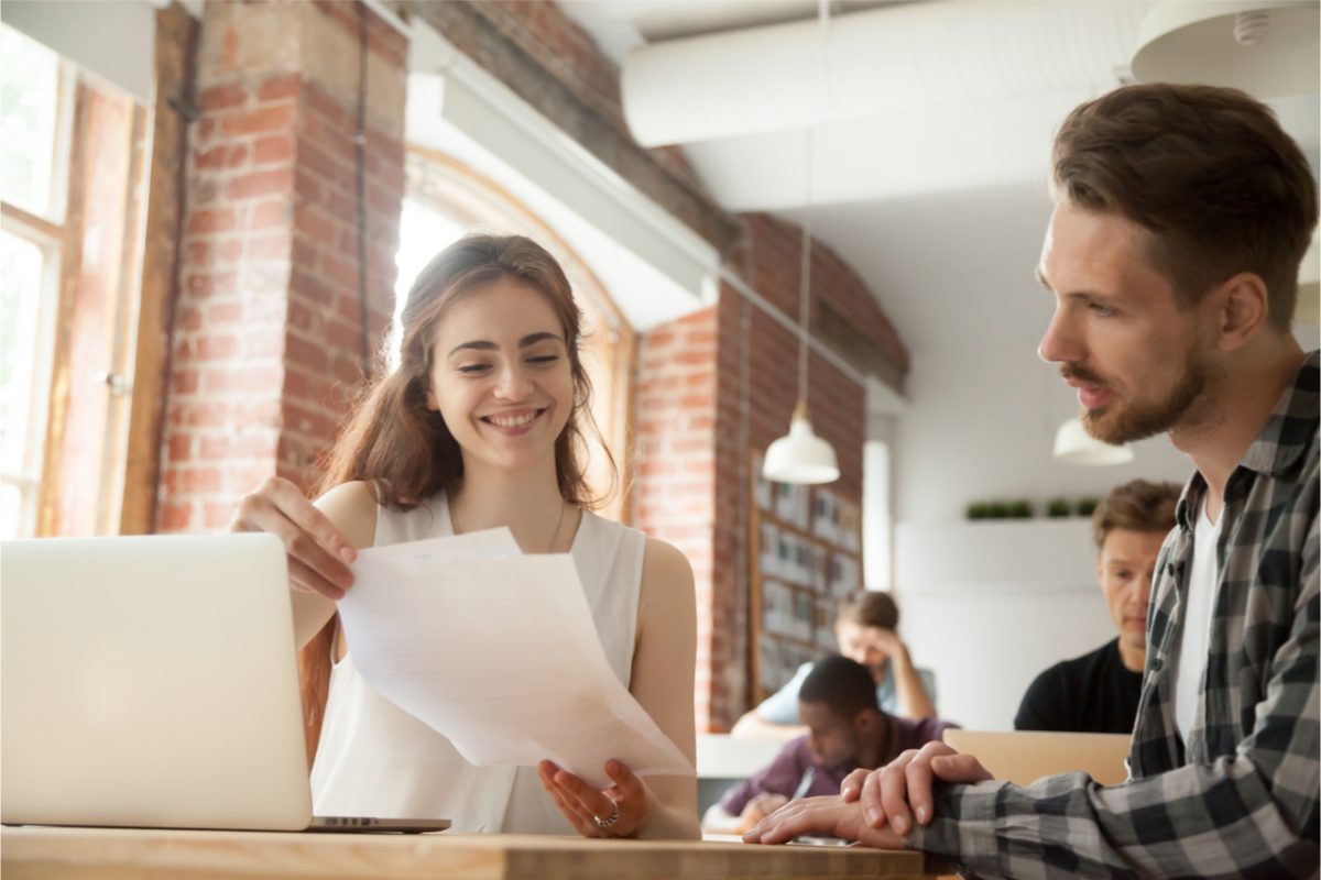 A young woman showing a colleague some paperwork.