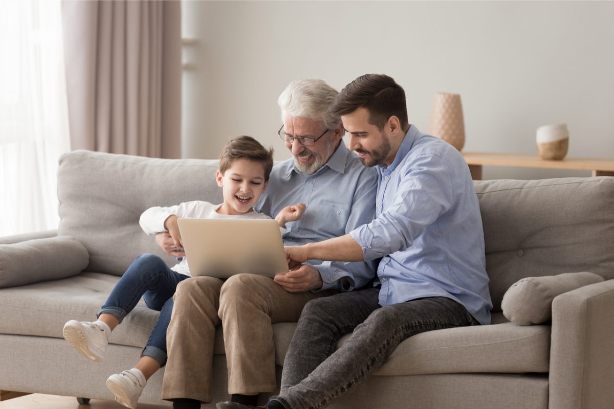 A grandfather using a laptop with his adult son and grandchild.