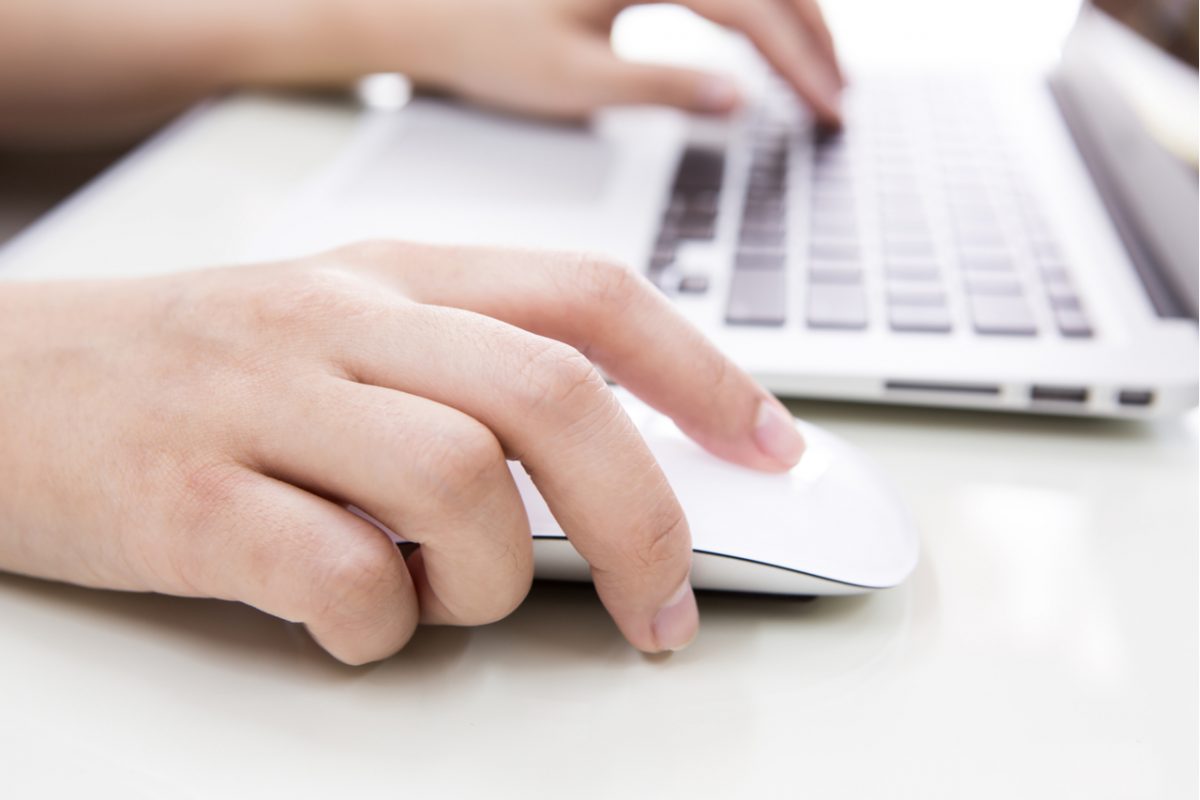 A person typing on a laptop keyboard and using a mouse.