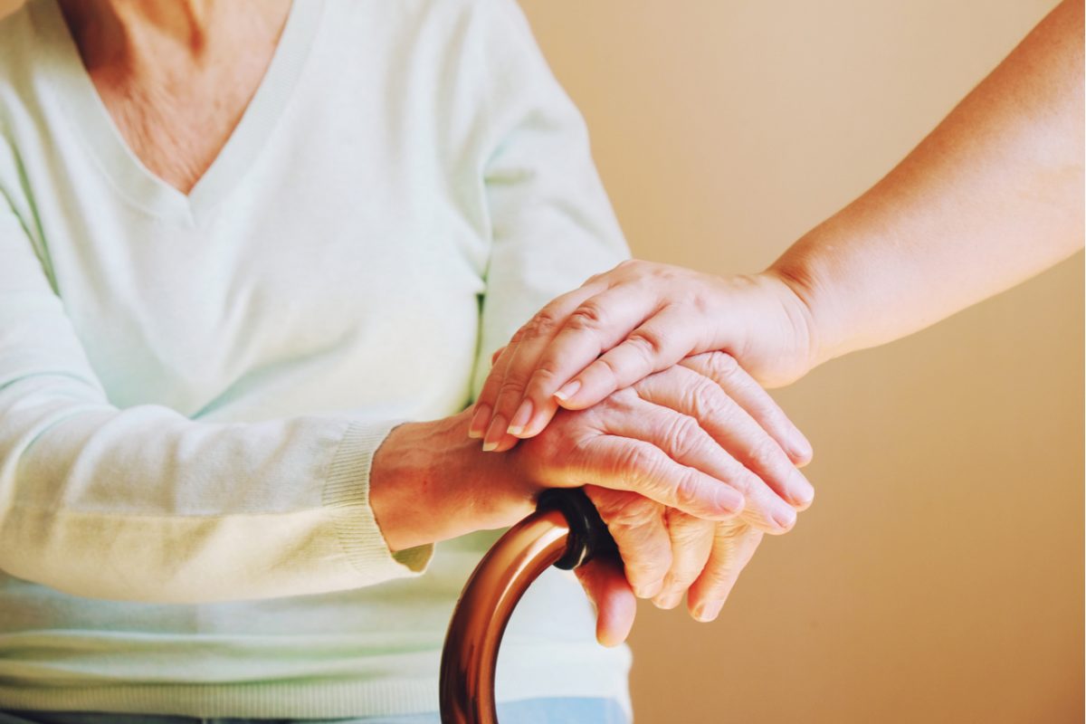 Close-up of someone holding hand the hand of an older woman with a walking aid.