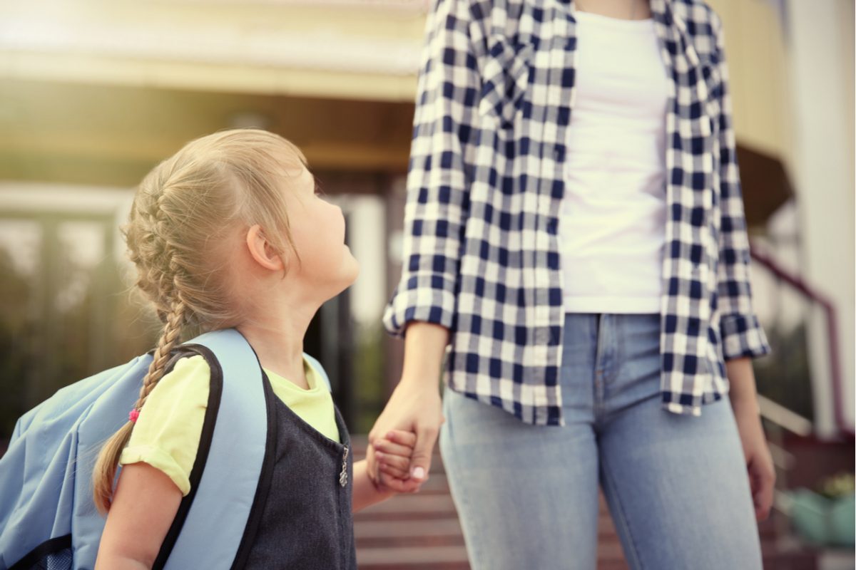 A mother and daughter holding hands as they walk to school.