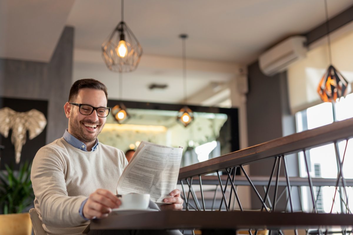 A man reading a newspaper while drinking coffee.