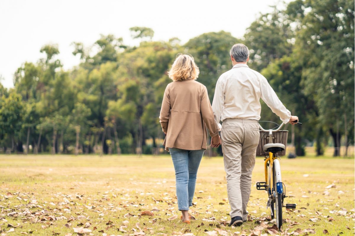 A couple walking through a park and pushing a bike.