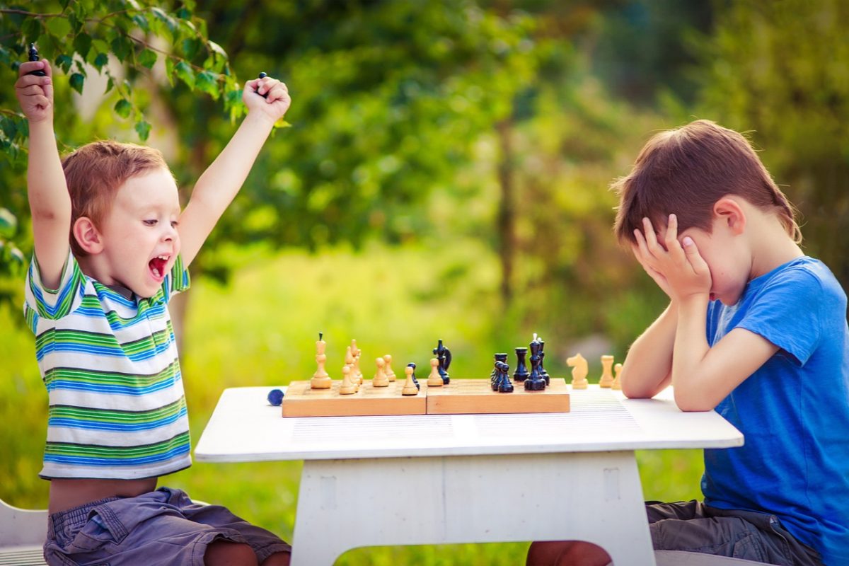 two boys playing chess, one has just won the game and is celebrating