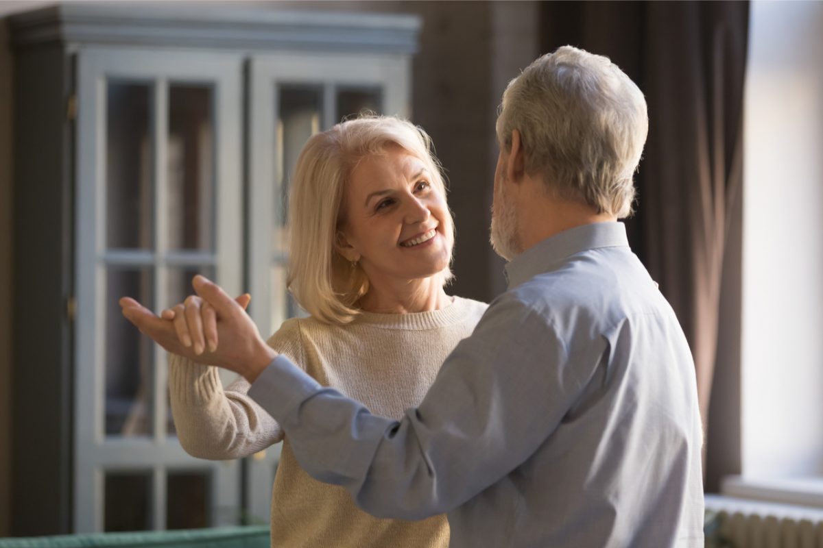 A smiling senior couple dance in their living room