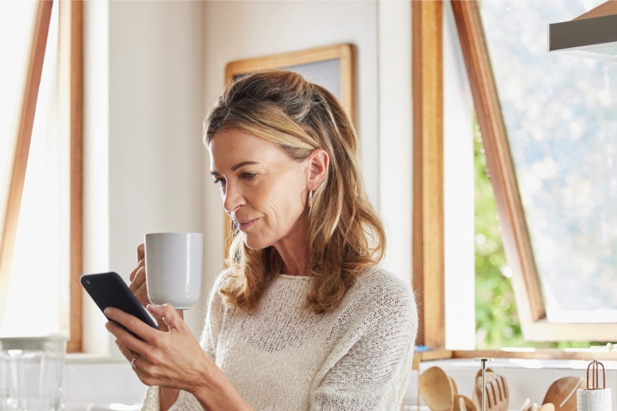 A woman drinking a coffee while looking at her phone.