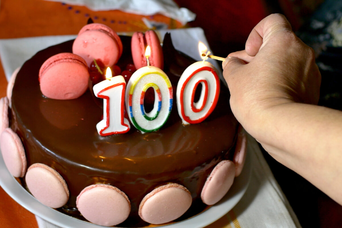 Someone lighting candles on a 100th birthday cake.