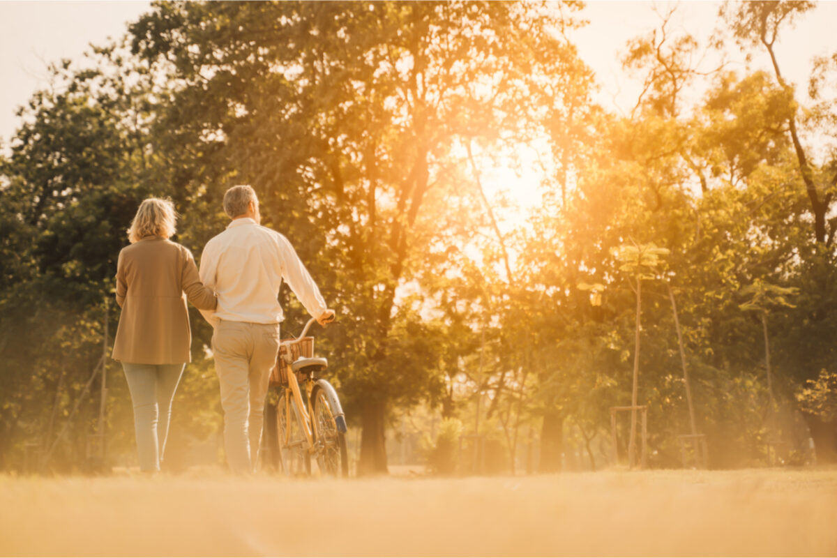 A couple walking in a park and pushing a bike.