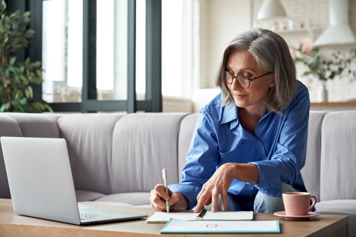 A woman using a laptop and writing notes.